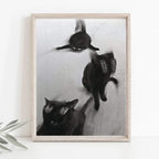 Black and white art print depicting three cats in motion, displayed on a white surface against a white wall with a small plant leaf visible at the bottom left.