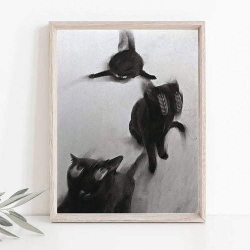 Black and white art print depicting three cats in motion, displayed on a white surface against a white wall with a small plant leaf visible at the bottom left.