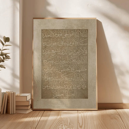 Framed artwork with Arabic calligraphy on a wooden floor with books and a plant.