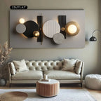 A modern abstract wall art piece with circular and rectangular geometric shapes in black, white, gray, and gold, mounted above a tufted sofa in a styled living room.