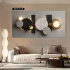 Modern abstract wall art featuring geometric circles, spheres, and rectangular forms in black, white, gray, and gold tones, displayed above a light beige sofa in a styled living room setting.