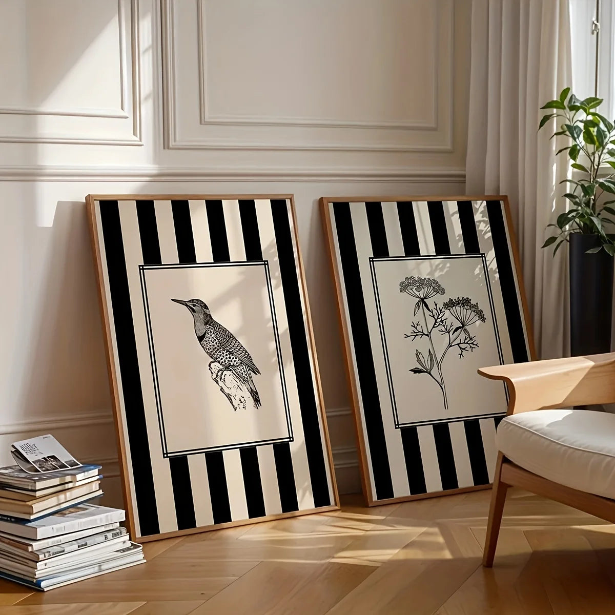 Two framed black and white artworks on a wooden floor with a chair and books in the background.