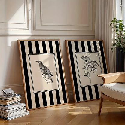 Two framed black and white artworks on a wooden floor with a chair and books in the background.