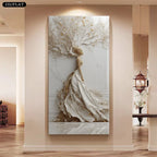 A large vertical wall art piece displayed in a hallway, featuring a stylized white and beige tree with flowing draped branches and trunk, rendered in a modern 3D sculptural style. The artwork is mounted on a beige wall above a wood floor, with interior decor visible in the background.