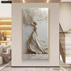 A large vertical wall art piece hangs on a beige wall in a modern interior. The artwork depicts a stylized white tree with flowing drapery-like branches and gold leaf accents, resembling a sculptural tree of life.