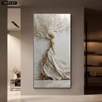 A tall vertical wall art piece displayed in a modern interior hallway. The artwork depicts a stylized white and beige tree with a flowing dress-like form and small gold leaf accents.