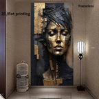 A large wall art print showing an abstract portrait of a woman's face in gold, black, and blue tones, displayed in a hallway next to a birdcage and a floor lamp. Text overlays read '2D/flat printing' and 'frameless'.