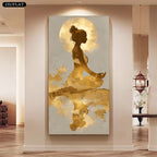 A large vertical canvas wall art print hanging in a modern interior hallway. The artwork depicts a meditating woman silhouette in dark brown against a large gold moon, with gold watercolor-like brushstrokes and reflection below.