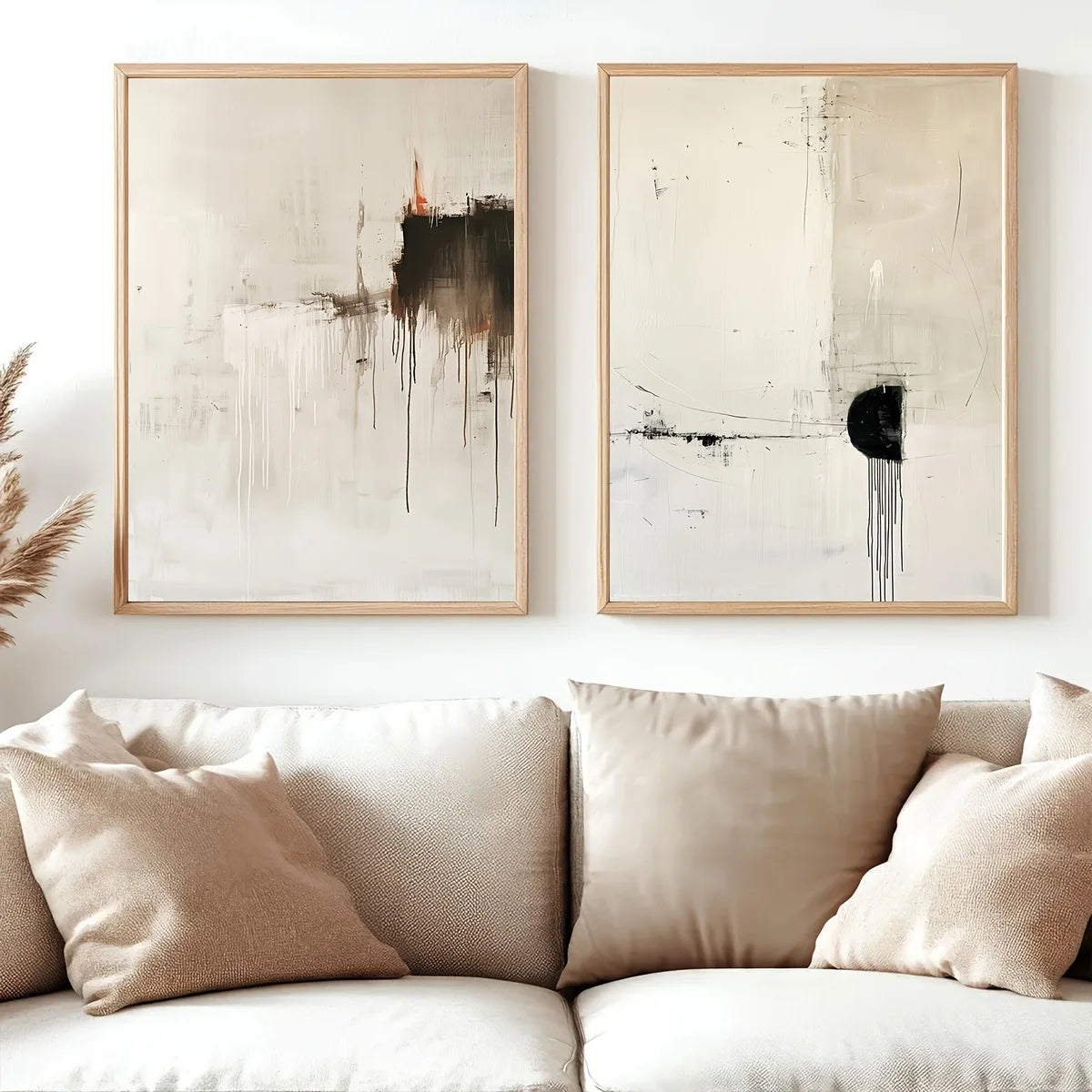 Two framed abstract wall art prints hang above a beige sofa with matching pillows in a softly styled living room.