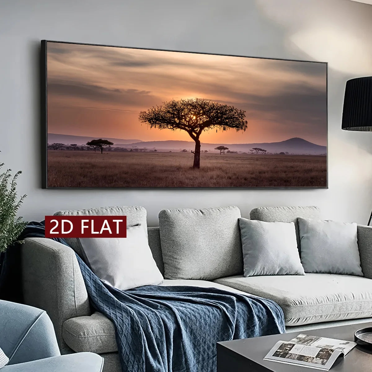 A large rectangular wall art print showing a savanna landscape with a lone tree at sunset, displayed above a light gray sofa in a modern living room. The print has a thin dark frame, and a red label reading '2D FLAT' appears near the lower left of the artwork.