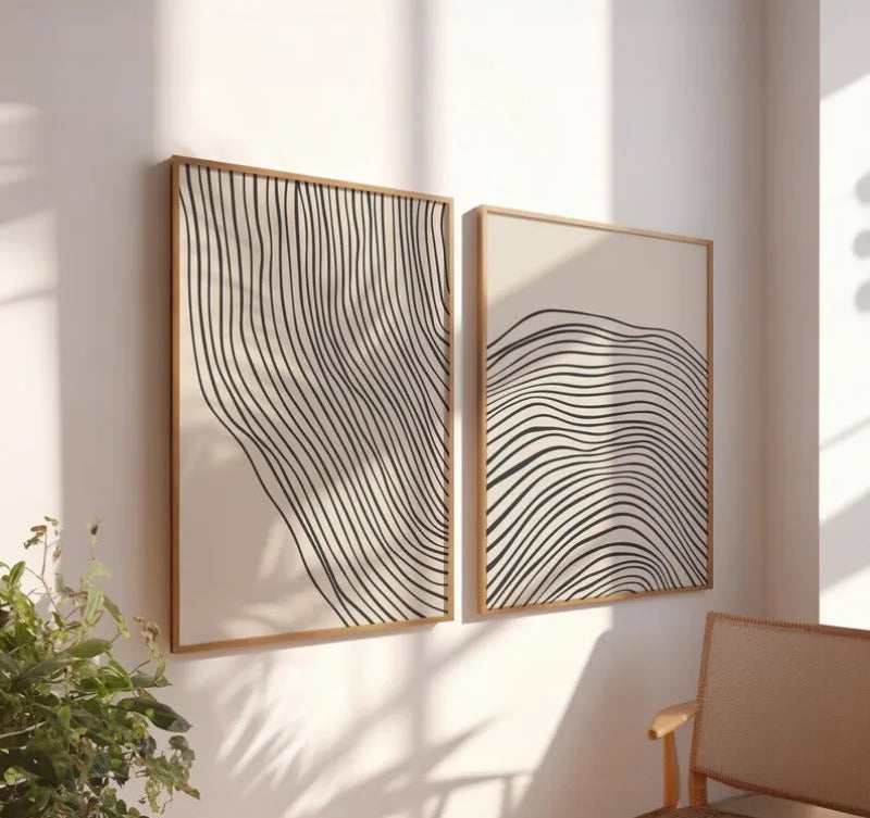 Two abstract wall art pieces with wavy lines on a light wall, with a plant and chair in the foreground.
