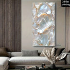 A vertical canvas wall art print featuring an abstract pearlescent floral or shell-like pattern in white, cream, and soft gold tones, displayed above a modern gray sofa in a styled living room. A small text overlay in the top right reads '2d flat printing'.