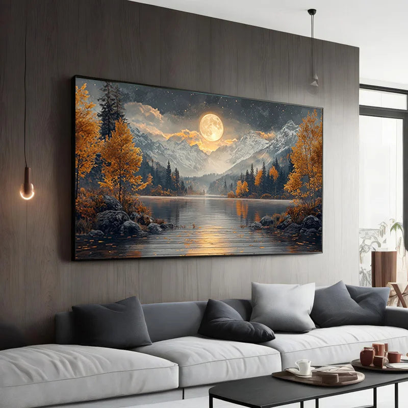A large landscape wall art print hangs above a white sofa in a modern living room. The artwork depicts a moonlit mountain lake scene with golden autumn trees, dark rocks, and snowy peaks reflected in the water.