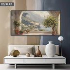 A horizontal canvas print depicting a scenic Italian coastal town with lemon trees and mountains, displayed on a wall above a modern white sofa in a styled living room.