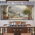 A large framed wall art print depicting a scenic coastal town with mountains, water, and lemon trees, displayed above a wooden dining table in a styled interior.