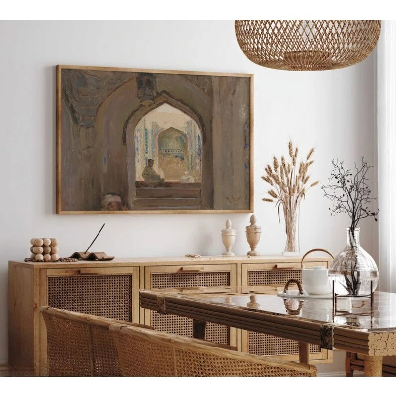 A framed art print depicting an arched architectural interior hangs on a white wall above a light wood credenza in a styled dining room setting.