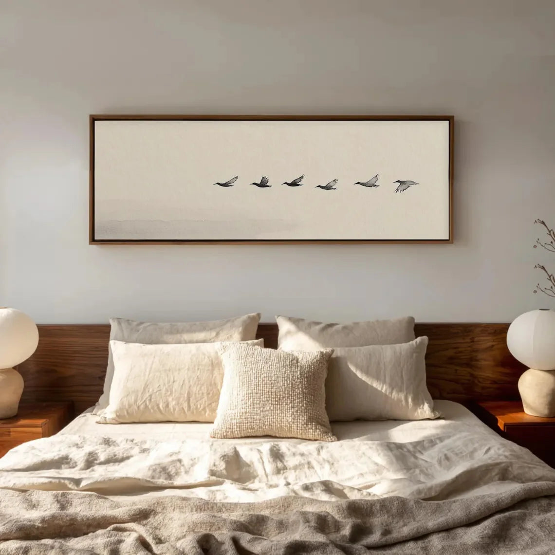 Framed artwork above a bed with pillows and a wooden headboard.