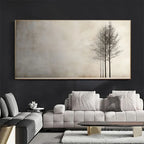 A large wall art piece hangs above a light gray sofa in a modern living room. The artwork shows a minimalist beige background with three dark, bare trees on the right side.