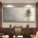 A large horizontal wall art piece hangs above a dark wood console in an office setting. The artwork shows a minimalist scene with three thin dark trees against a soft gray and beige background.