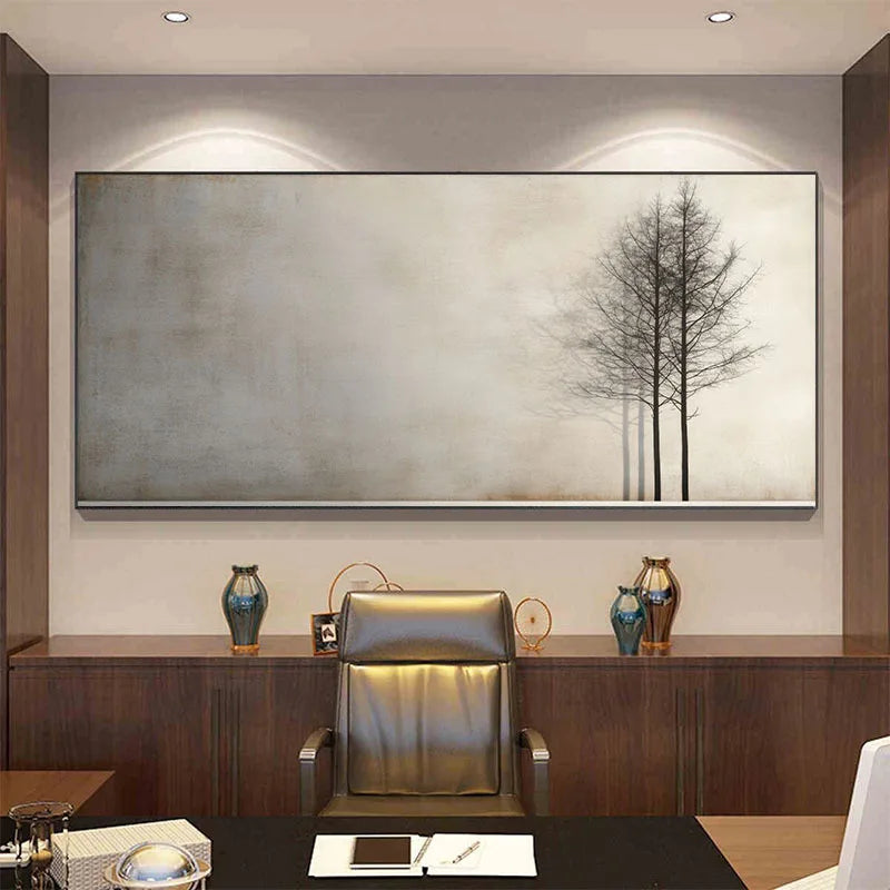 A large horizontal wall art piece hangs above a dark wood console in an office setting. The artwork shows a minimalist scene with three thin dark trees against a soft gray and beige background.