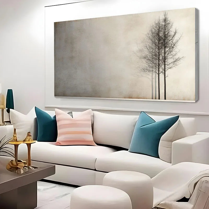 A large rectangular wall art print showing two bare trees against a textured beige and gray background, displayed above a white sofa with teal and pink pillows in a modern living room.