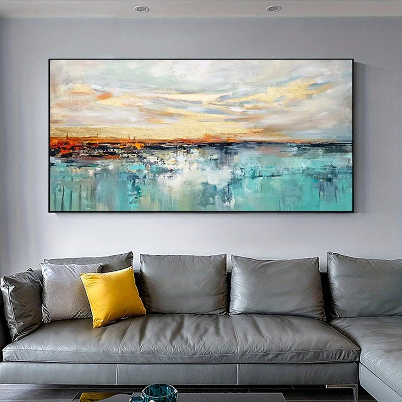 A large framed abstract canvas painting of a coastal sunset hangs on a light gray wall above a modern gray leather sectional sofa with a yellow accent pillow.