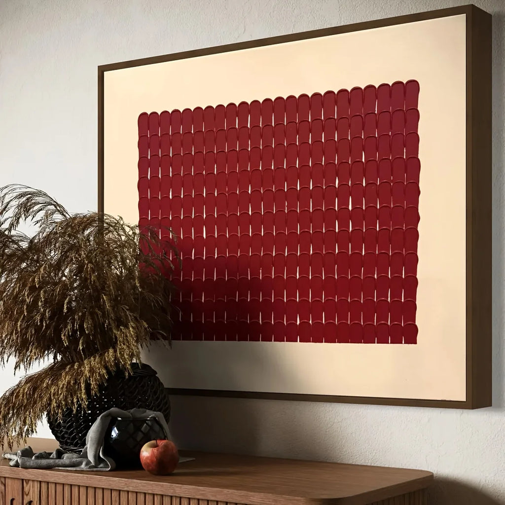 Framed abstract artwork with a red pattern on a beige background, displayed on a wall above a wooden console table.