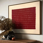 Framed abstract artwork with a red pattern on a beige background, displayed on a wall above a wooden console table.