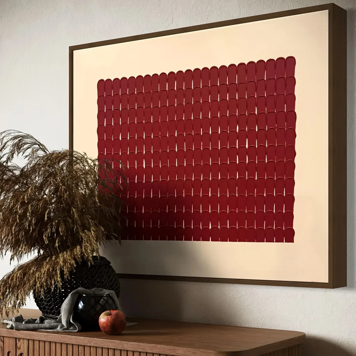 Framed abstract artwork with a red pattern on a beige background, displayed on a wall above a wooden console table.