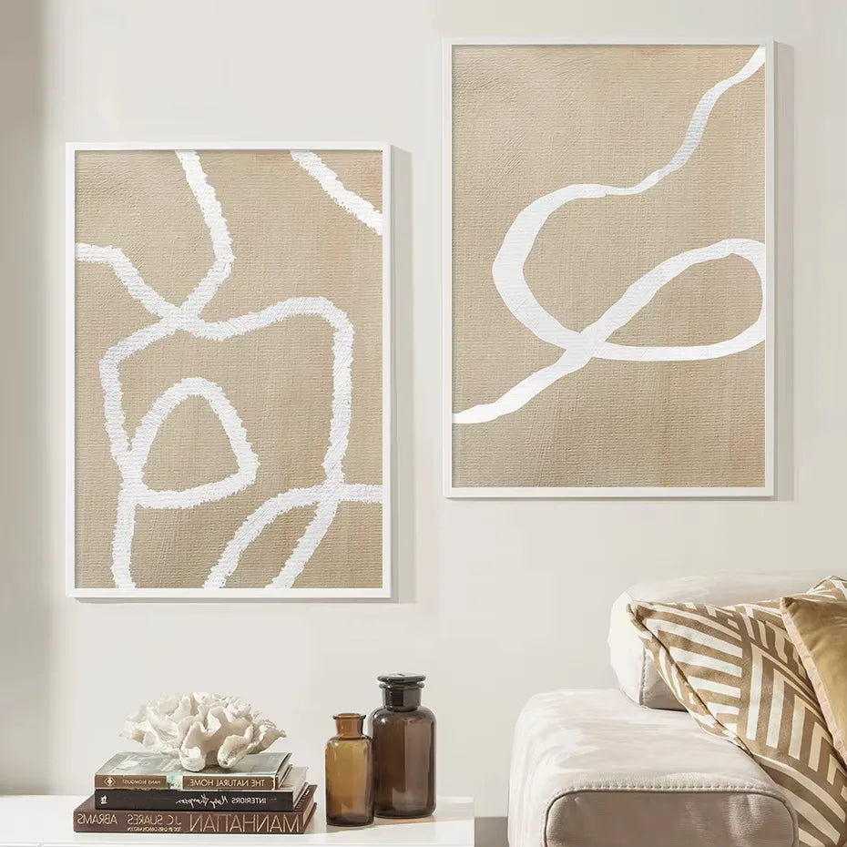 Two abstract canvas prints with white organic line art on a beige linen-textured background, displayed on a light wall above a sofa with decorative pillows and small bottles.