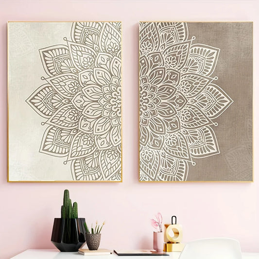 Two vertical framed wall art prints with intricate mandala designs hang on a light pink wall above a desk with small decor items including a cactus, books, and a pink candle holder.