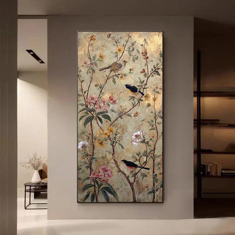 A vertical wall art piece featuring a floral and bird scene with birds perched on branches among pink, yellow, and white flowers, displayed on a light gray wall in a modern interior setting.