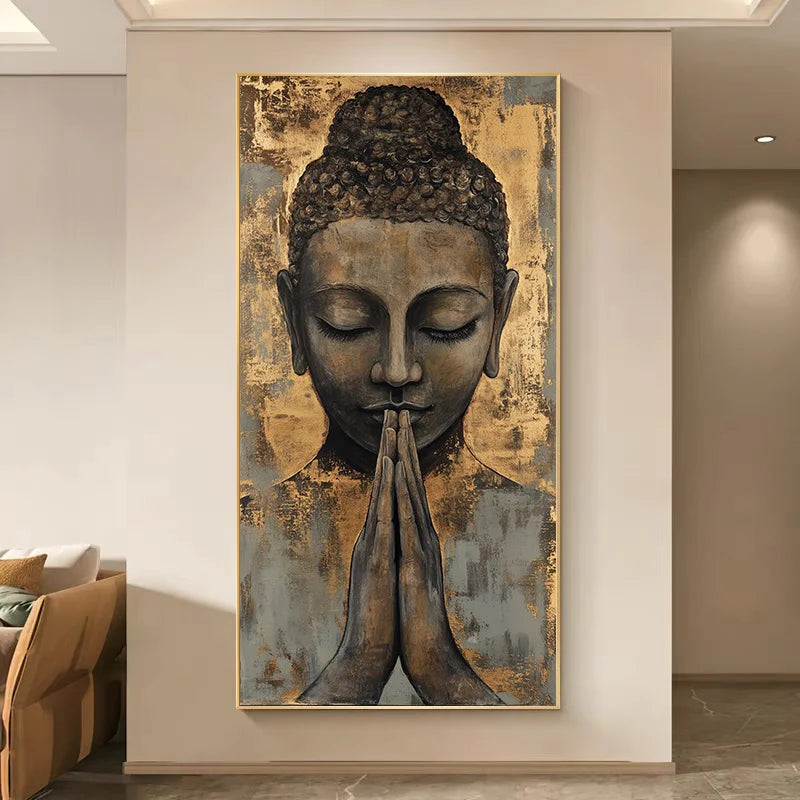 A vertical framed wall art print showing a serene Buddha face with hands in prayer, displayed on a beige wall in a modern interior hallway.