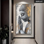 A vertical wall art print showing a serene Buddha figure in profile with hands in prayer, rendered in gray, white, and gold tones. The artwork is displayed hanging on a wall in a modern hallway with a plant at left and a black '2D/FLAT' label in the top-right corner.