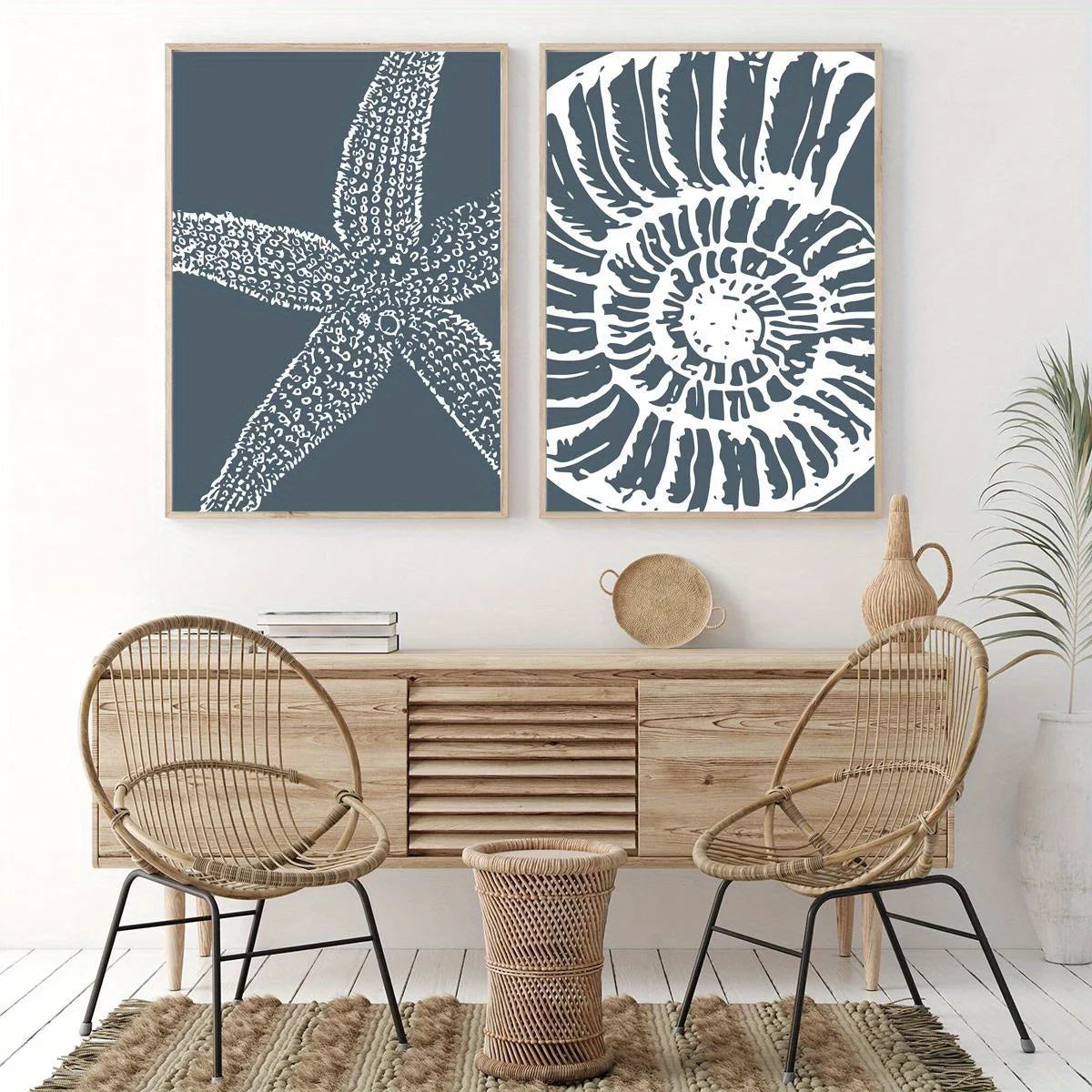 Two framed wall art prints hang above a light wood console in a styled interior. The left print shows a white starfish on a dark blue-gray background, and the right print shows a white spiral shell pattern on the same blue-gray background.