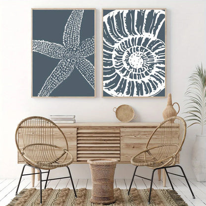 Two framed wall art prints hang above a light wood console in a styled interior. The left print shows a white starfish on a dark blue-gray background, and the right print shows a white spiral shell pattern on the same blue-gray background.
