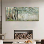 A wide rectangular framed painting of a misty forest with tall trees hangs above a fireplace filled with stacked firewood in a modern living room setting.